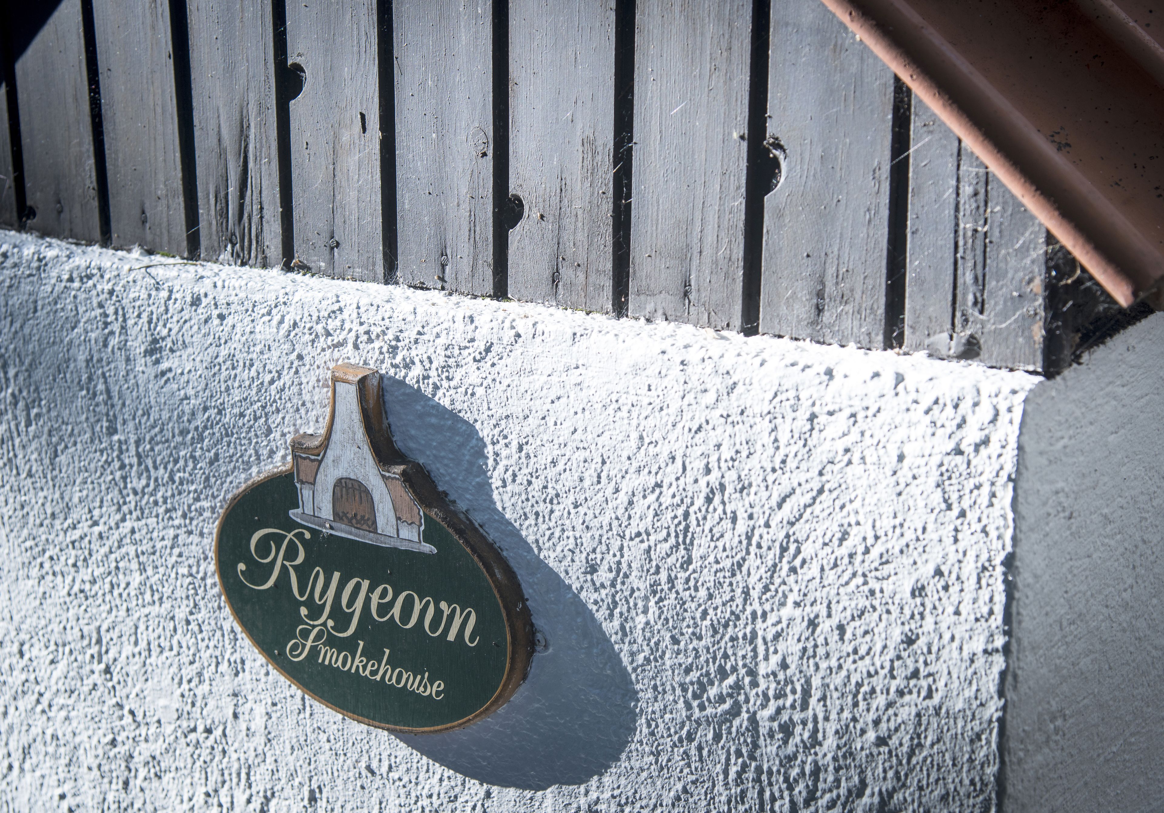 A wooden sign with the text "Rygeown Smokehouse" mounted on a white textured wall.