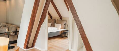 A loft bedroom with exposed wooden beams, a bed with pillows, a desk, and a sofa.