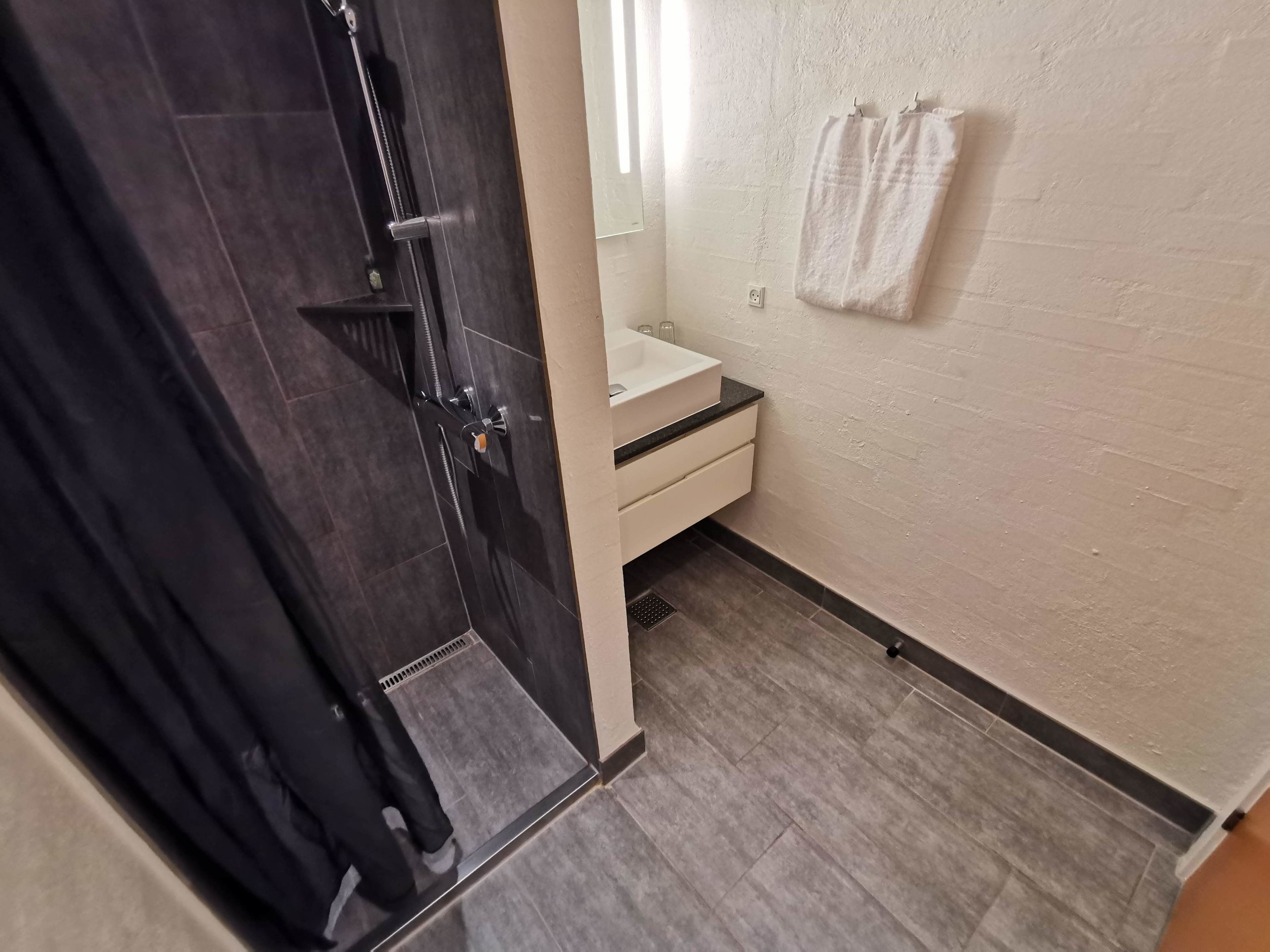 A bathroom with a dark shower, a white sink, and a towel hanging on the wall.