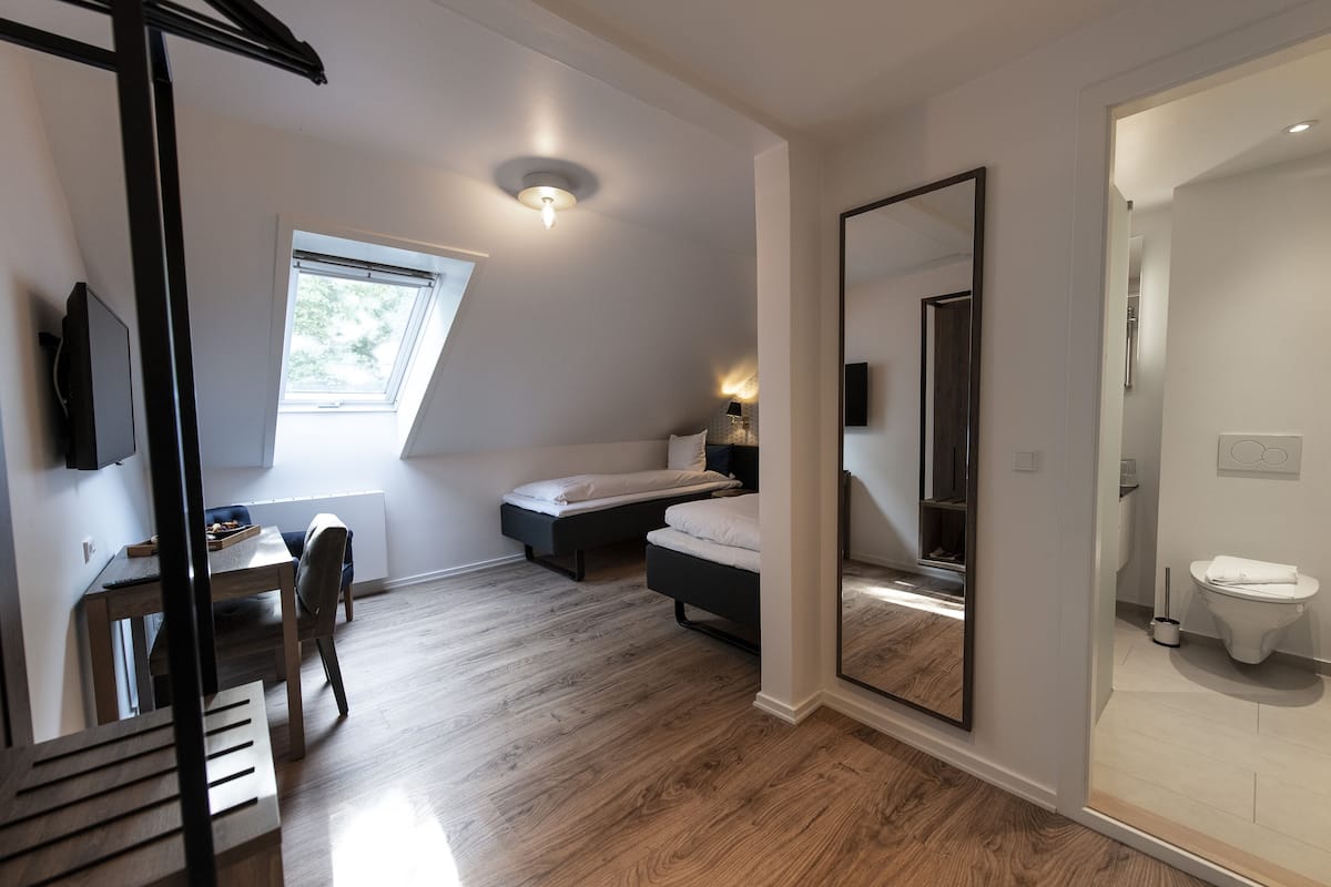 A bedroom with a bed, a desk, and a chair. There is a window and a door leading to a bathroom.