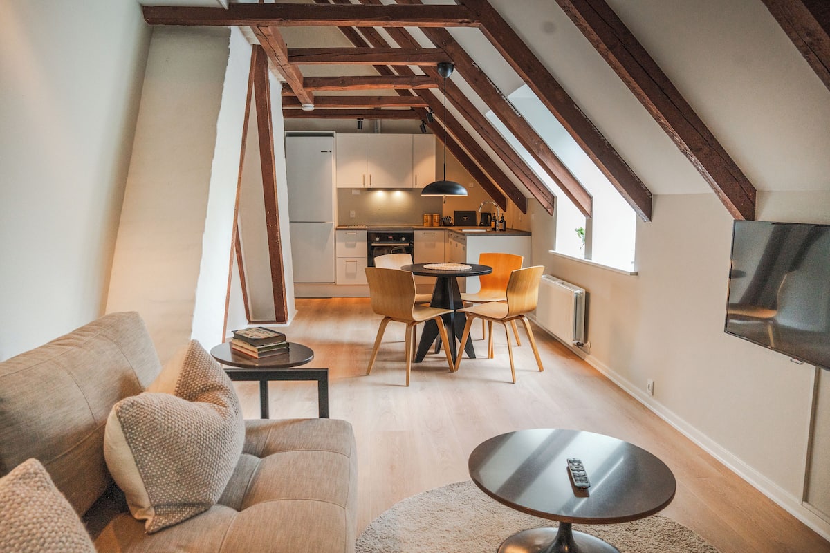 A cozy loft apartment with a dining area, kitchen, and a TV mounted on the wall.