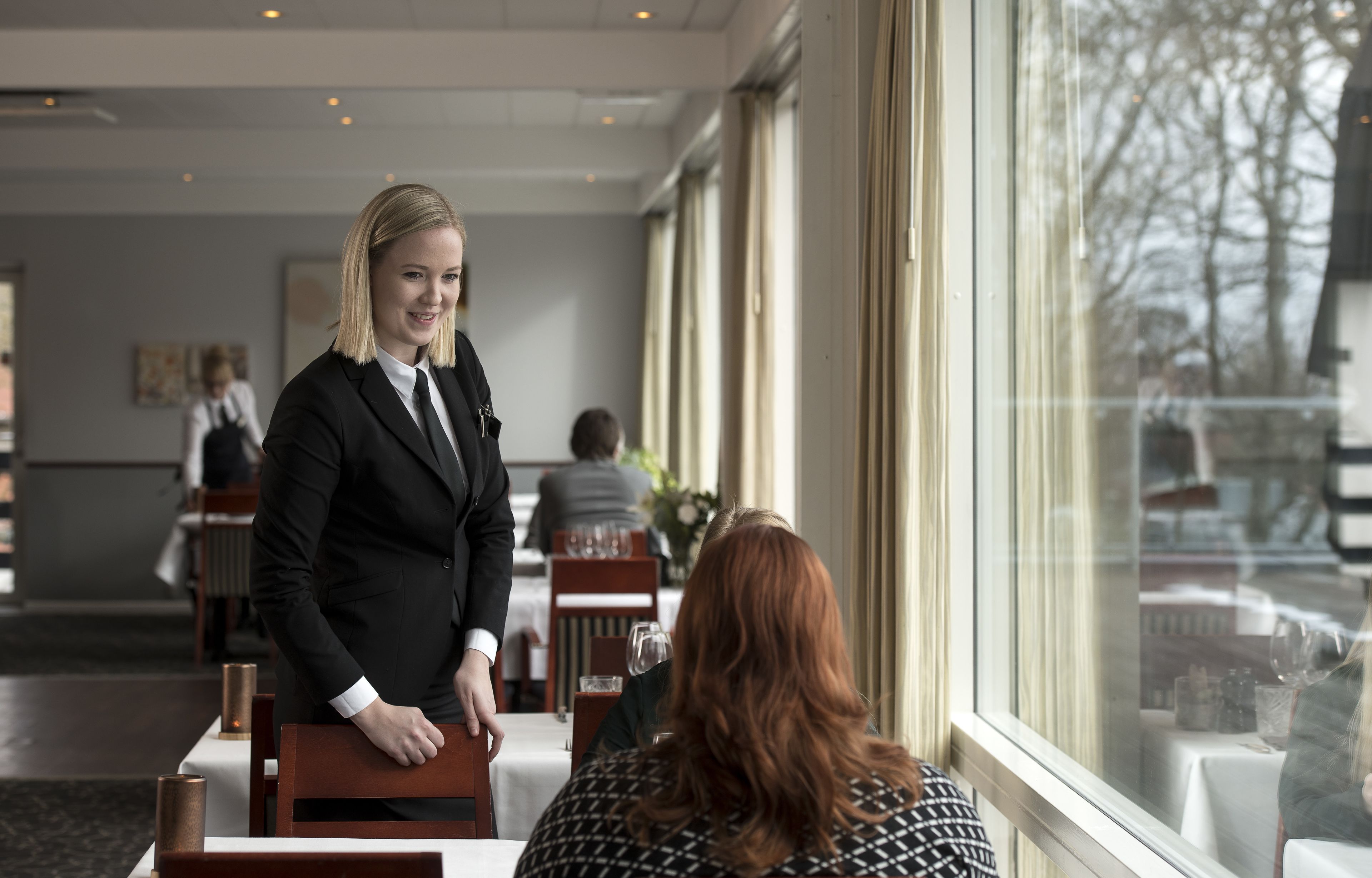 A hotel lobby with a reception desk, dining area, and large windows offering a view of the outside.