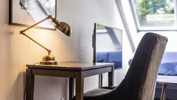 Un espacio de trabajo con escritorio, silla, lámpara de escritorio, monitor de computadora y ventana con vistas.
