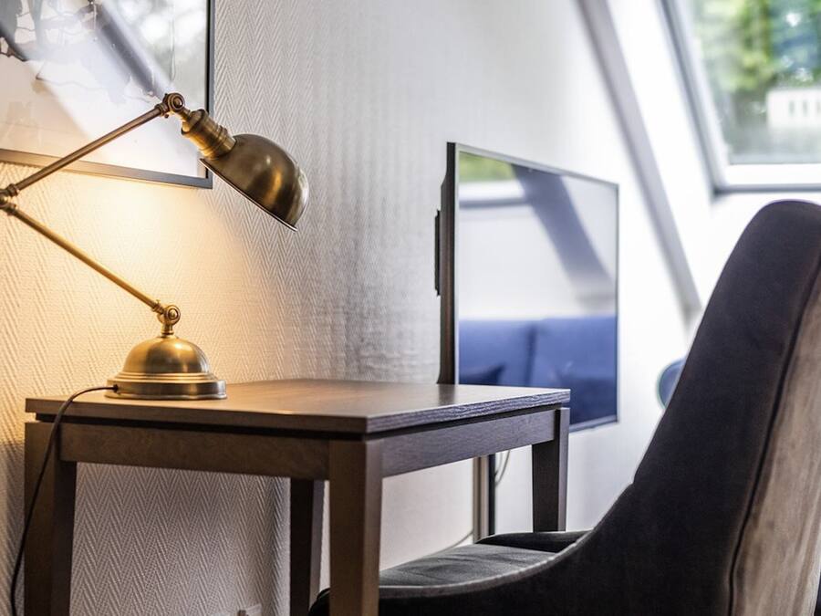A workspace with a desk, a chair, a desk lamp, a computer monitor, and a window with a view.