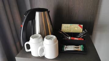 Une petite table avec une machine à café, deux tasses blanches et un plateau contenant des sachets de café et des ustensiles.