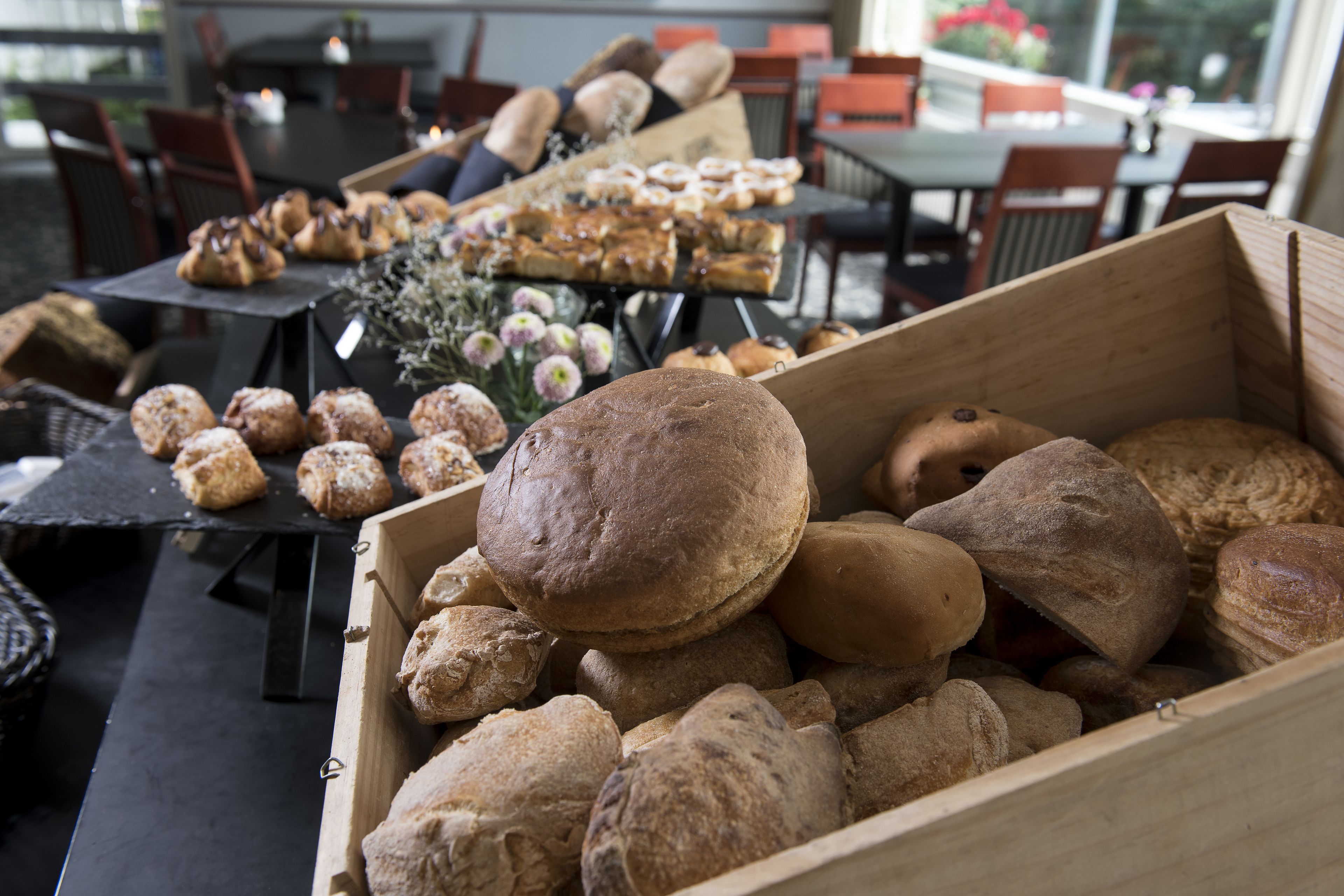 A wooden crate filled with various types of bread and pastries, placed on a table in a restaurant setting.