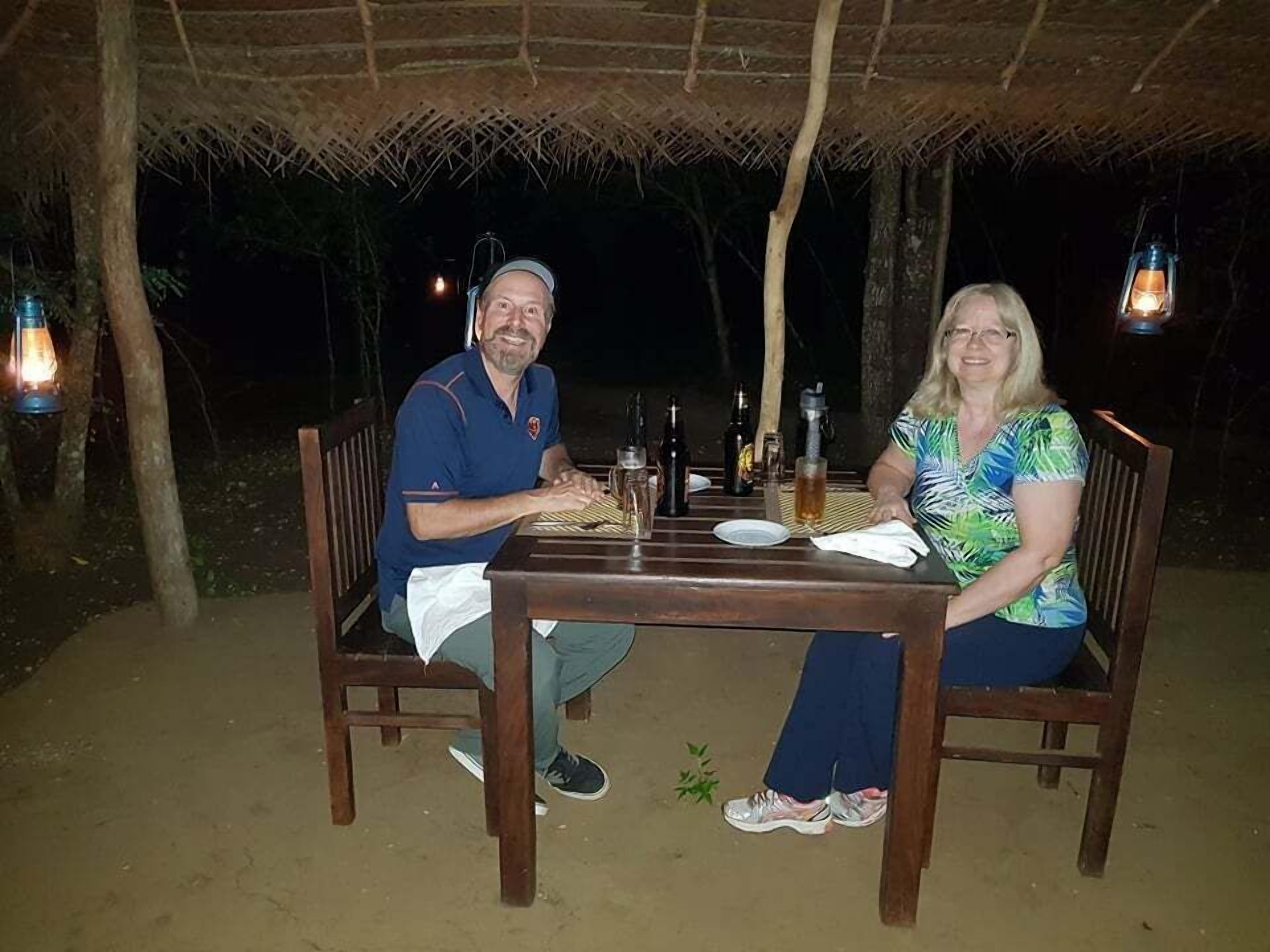 Two people seated at a wooden table with a thatched roof overhead.