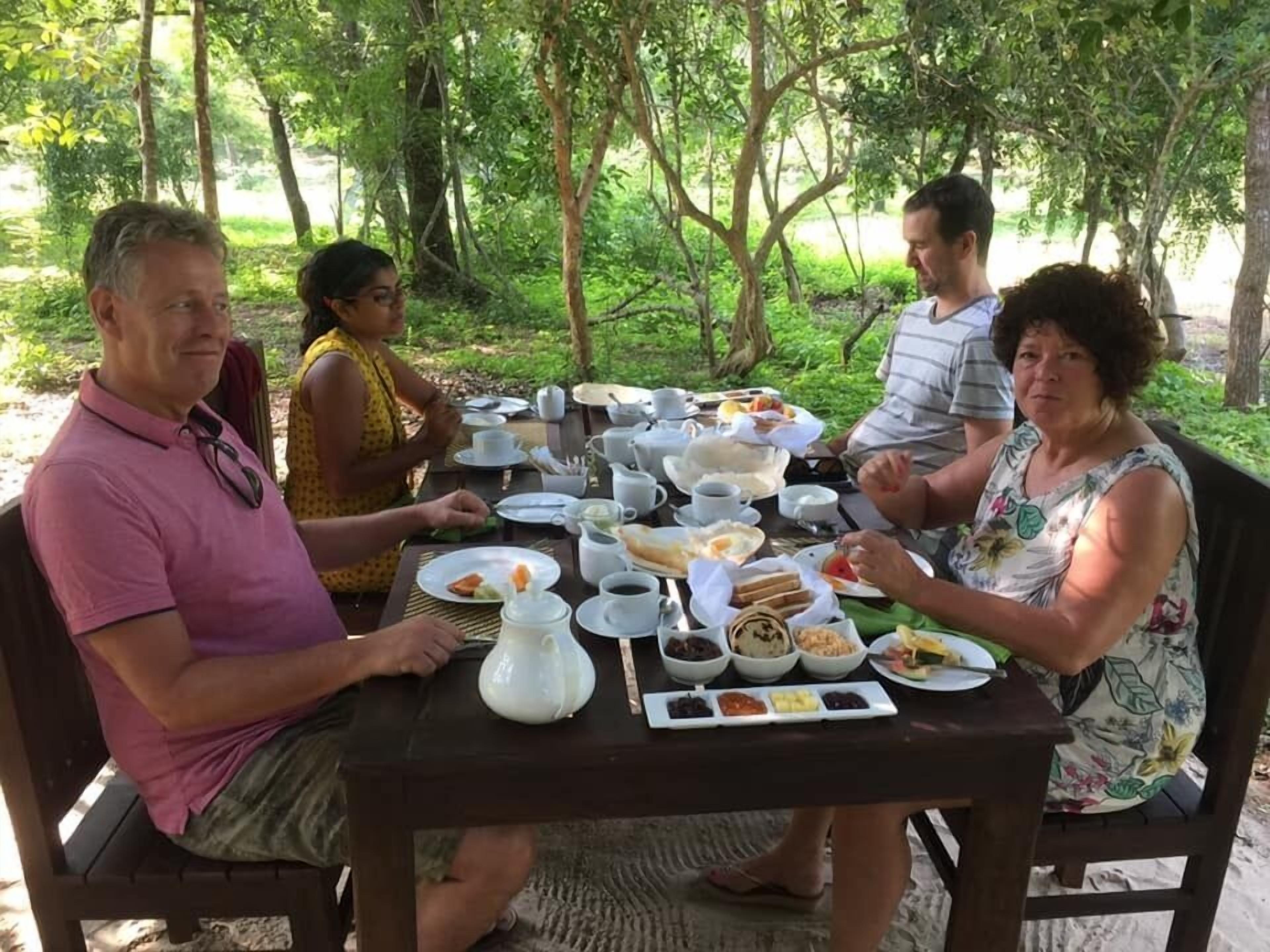A group of people dining at an outdoor table with various dishes and drinks.
