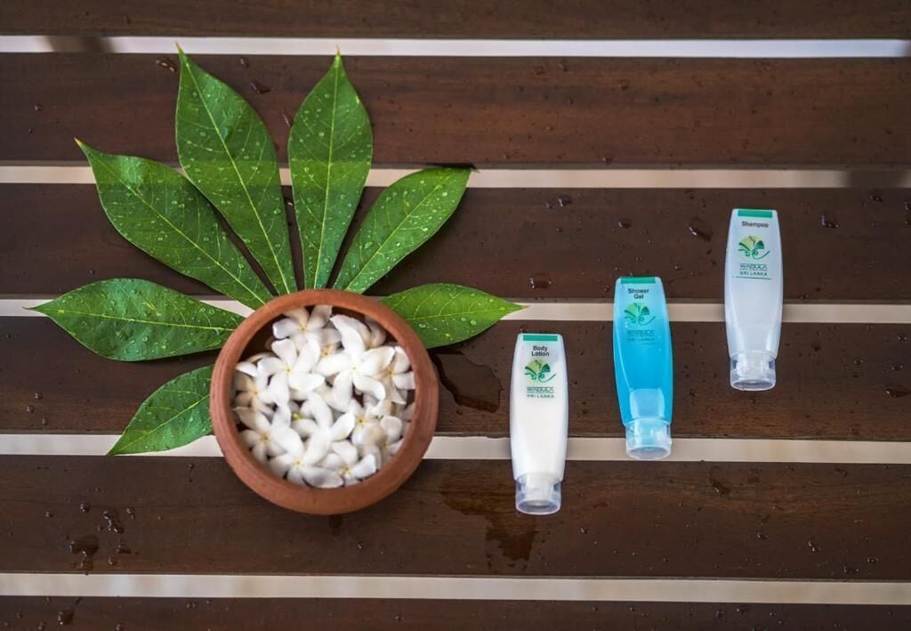 A wooden surface with a bowl of white flowers, green leaves, and three toiletry items.