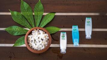 Una superficie de madera con un cuenco de flores blancas, hojas verdes y tres artículos de tocador.