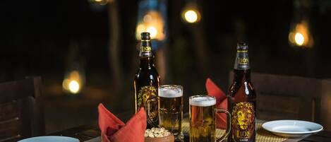 A table set for two with two beer bottles, two glasses, a bowl of snacks, and a red napkin.