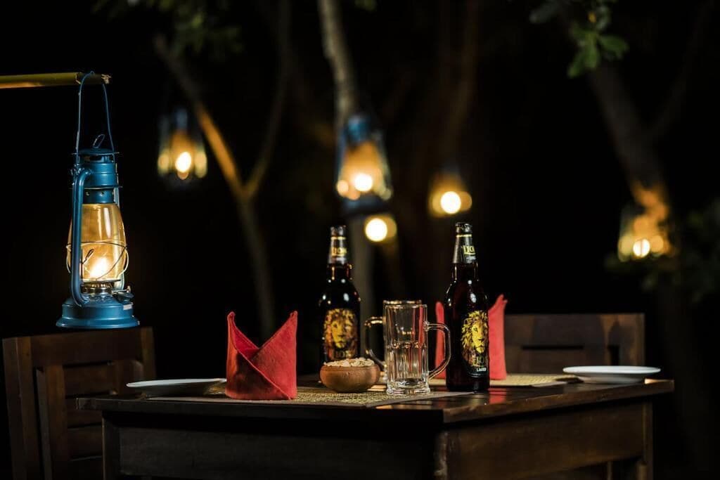 Ein Tisch im Freien bei Nacht, mit einer Laterne, Flaschen, einem Glas und einer Schüssel.