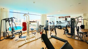 A gym with various exercise equipment, a punching bag, and a view of a swimming pool through large windows. - Mirage Bab Al Bahr Hotel (Dhadnah)