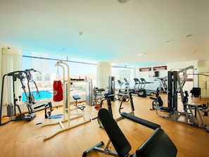A gym with various exercise equipment, a punching bag, and a view of a swimming pool through large windows. - Mirage Bab Al Bahr Hotel (Dhadnah)