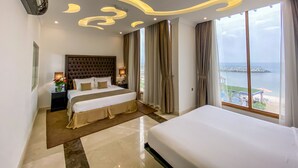 A modern hotel room with a large bed, a nightstand, a lamp, and a view of the sea. - Mirage Bab Al Bahr Hotel (Dhadnah)