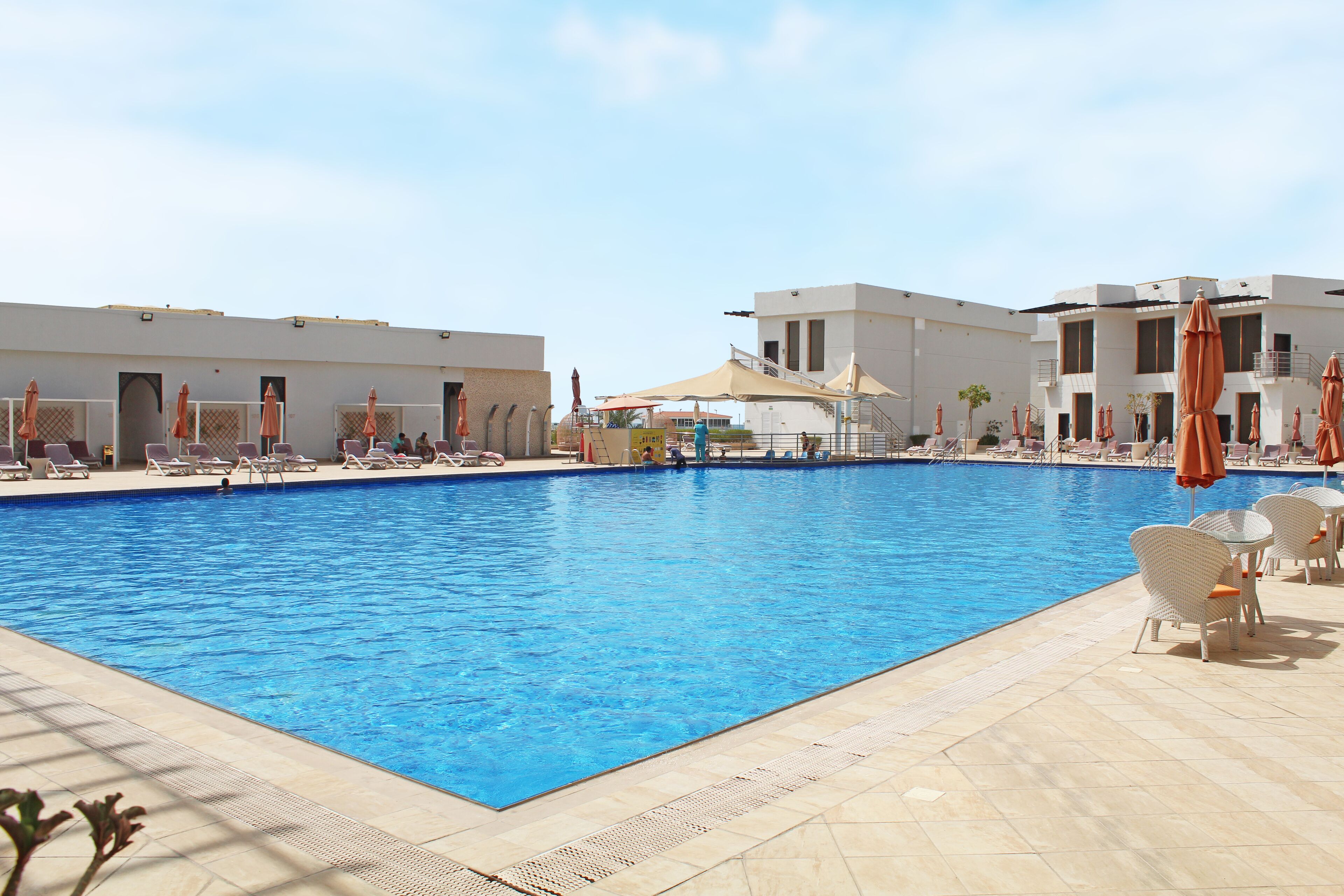 Una piscina con sillas de descanso y sombrillas, rodeada de edificios con balcones.