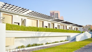 A modern building with a flat roof, a white exterior, and a green lawn area. - Mirage Bab Al Bahr Hotel (Dhadnah)
