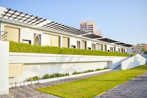 A modern building with a flat roof, a white exterior, and a green lawn area. - Mirage Bab Al Bahr Hotel (Dhadnah)