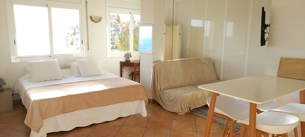 A bedroom with a bed, a sofa, a table, and a desk.