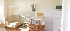 A compact living space with a sofa, a small table with chairs, a television, and a microwave. - Roses: Loft with private terrace and garden, magnificent sea view (Roses)