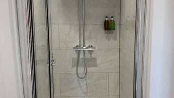 Un box de ducha moderno con puerta de cristal, cabezal de ducha de mano y grifo empotrado.