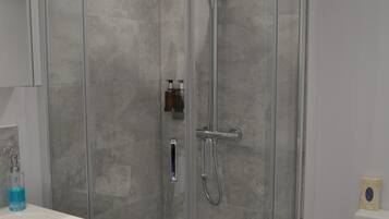A glass-enclosed shower with a handheld showerhead and a wall-mounted faucet.