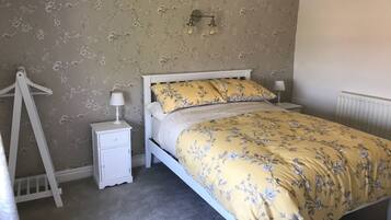 A bedroom with a bed, nightstands, a lamp, a radiator, and a hanging rack.