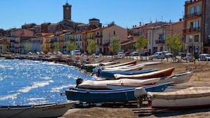 A coastal town with boats docked along the shore, buildings with balconies, and a prominent tower structure in the background. - B&B Il Cardellino (Porano)