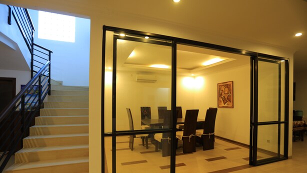 A modern interior with a staircase, a dining area with chairs and a table, and a large glass partition. - Pi Home Baciro (Yogyakarta)