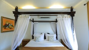A four-poster canopy bed with white bedding and decorative pillows, a wooden headboard, and a nightstand with a lamp. - Pi Home Baciro (Yogyakarta)