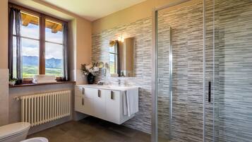 Un baño con inodoro, lavabo con espejo, ducha y ventana con cortinas.