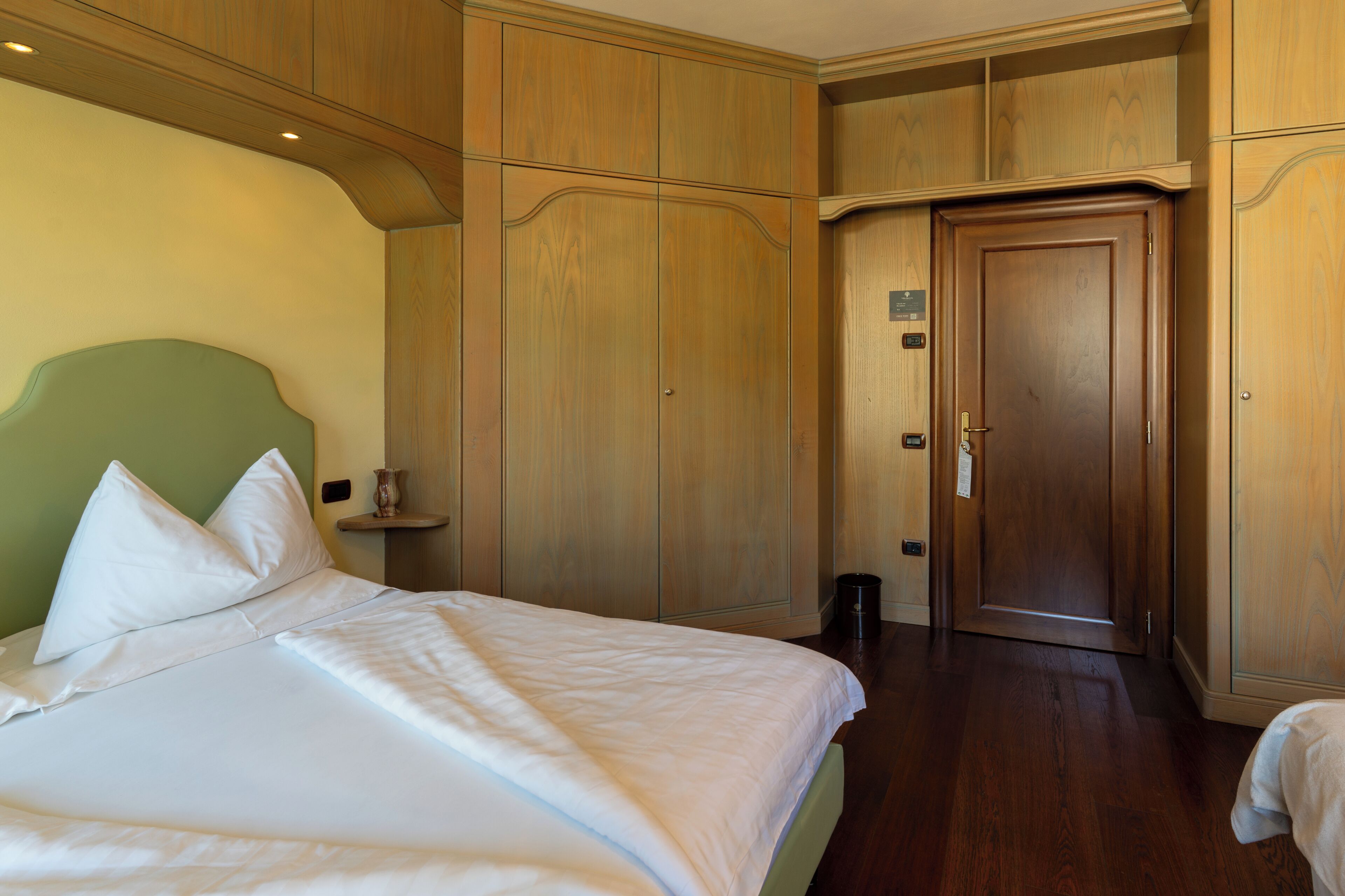 A hotel room with a large bed, wooden wardrobe, and a door.