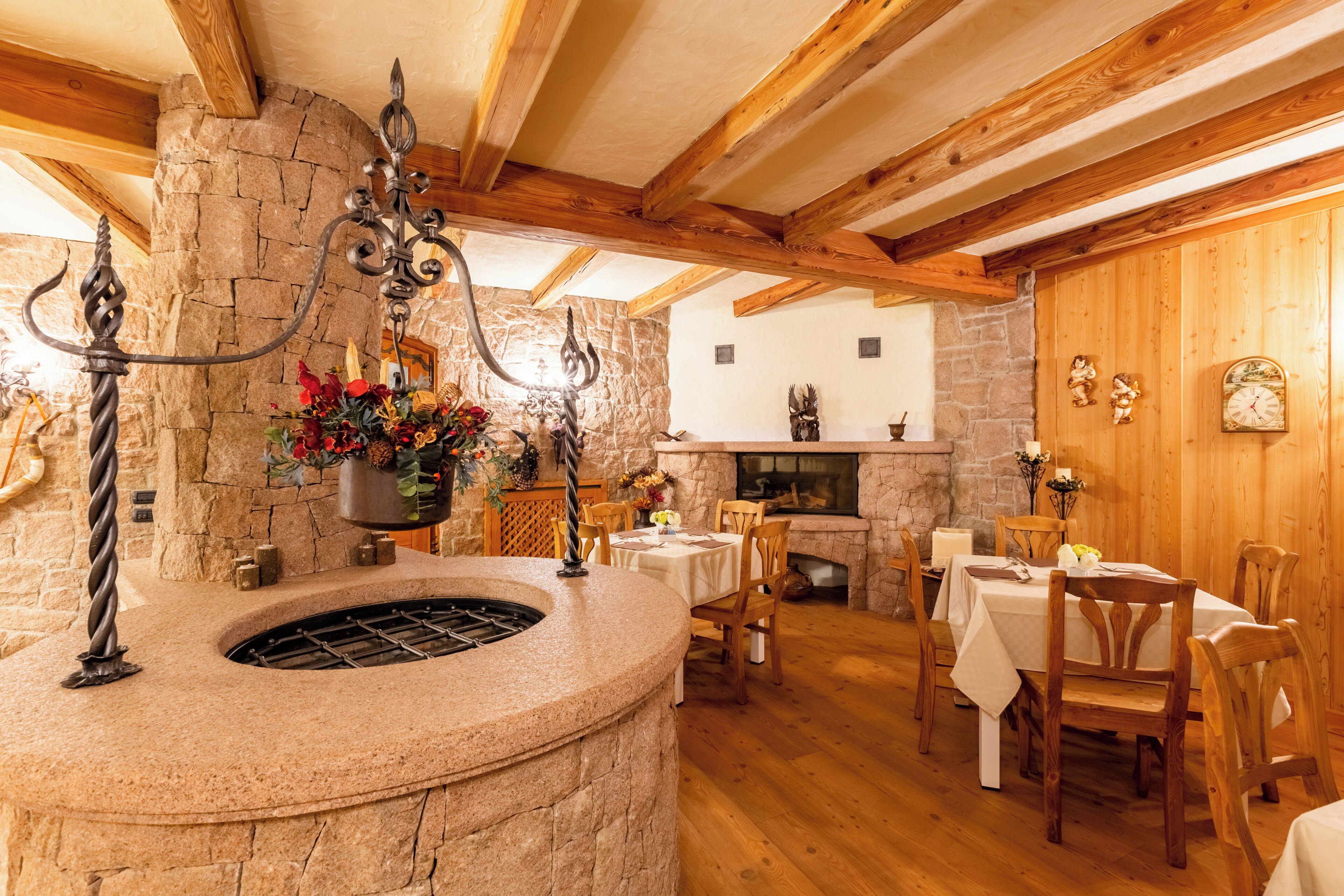 A stone fireplace, wooden beams, a dining area with tables and chairs, and a hanging light fixture.
