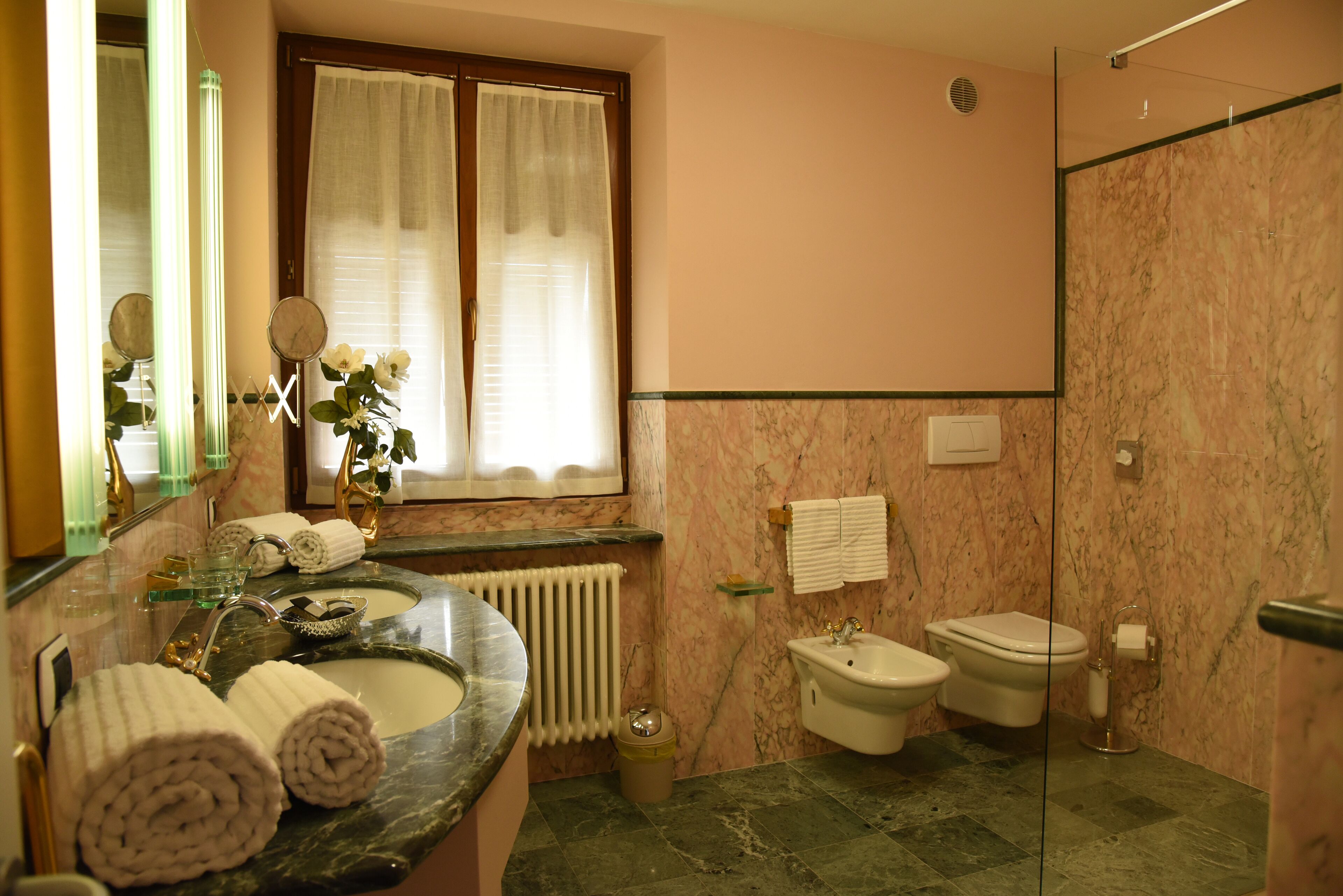 Ein Badezimmer mit Marmorwaschtisch, zwei Toiletten, einem Bidet und einer Duschkabine aus Glas.