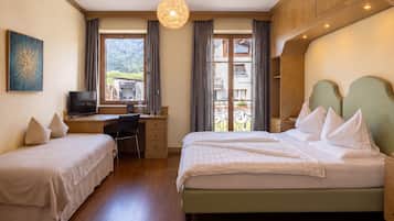 A hotel room with a bed, a desk, a chair, a TV, and a balcony with a view of the mountains.