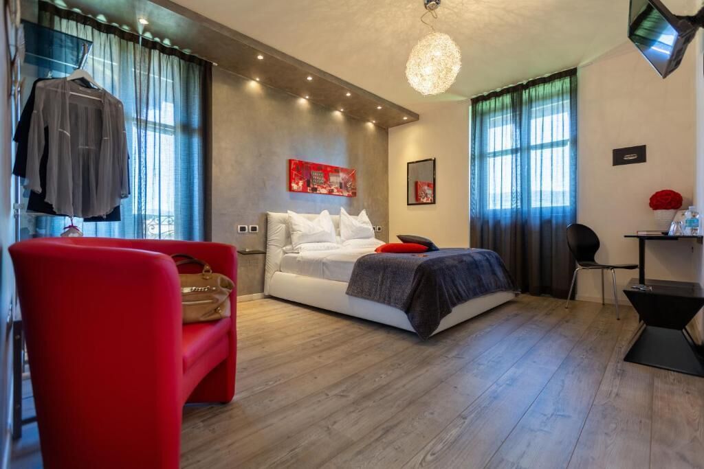 A modern hotel room with a bed, a red chair, a desk, and a chandelier.