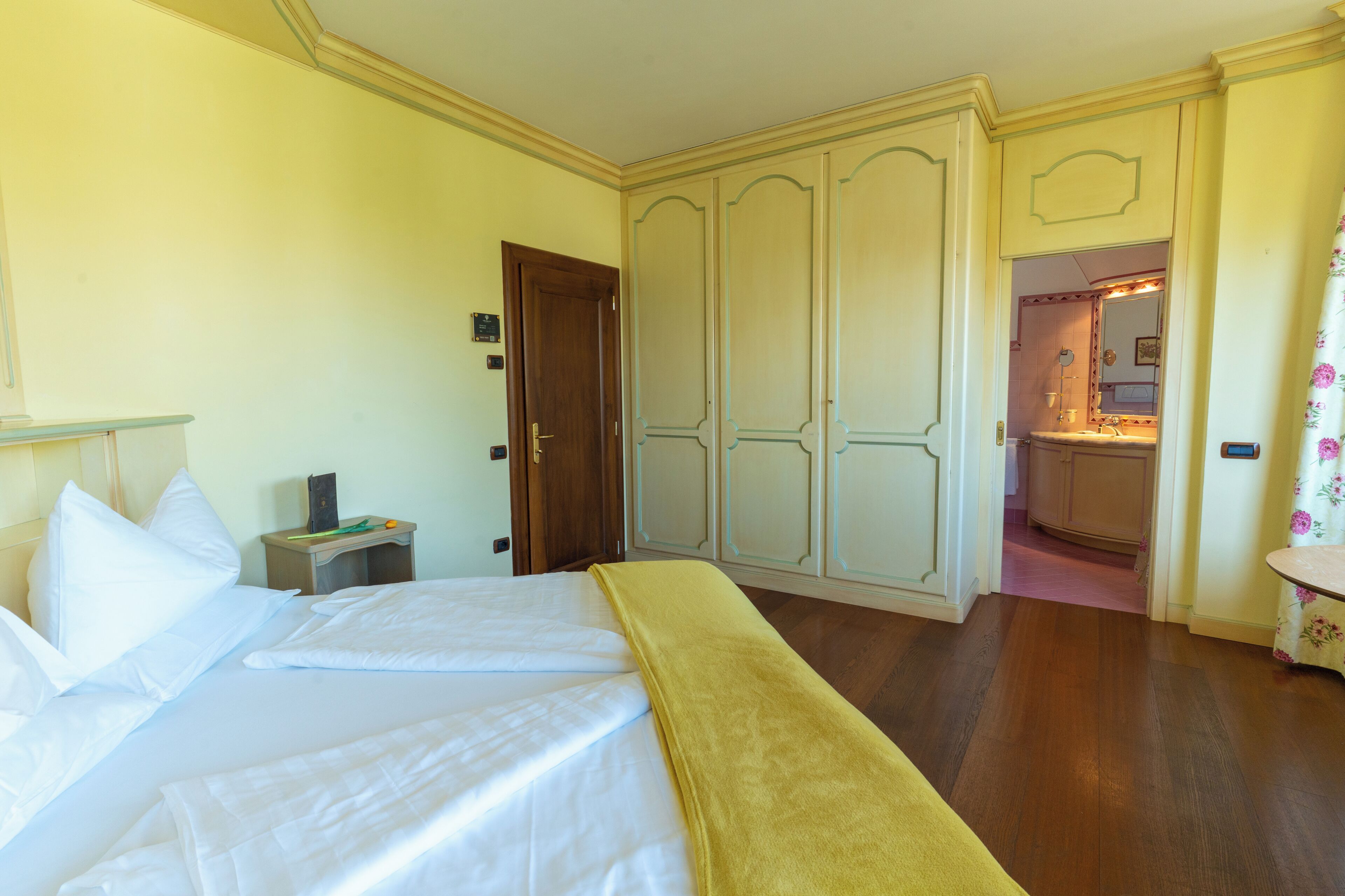 Quarto de hotel com cama, mesa de cabeceira, guarda-roupa e banheiro visível por uma porta aberta.