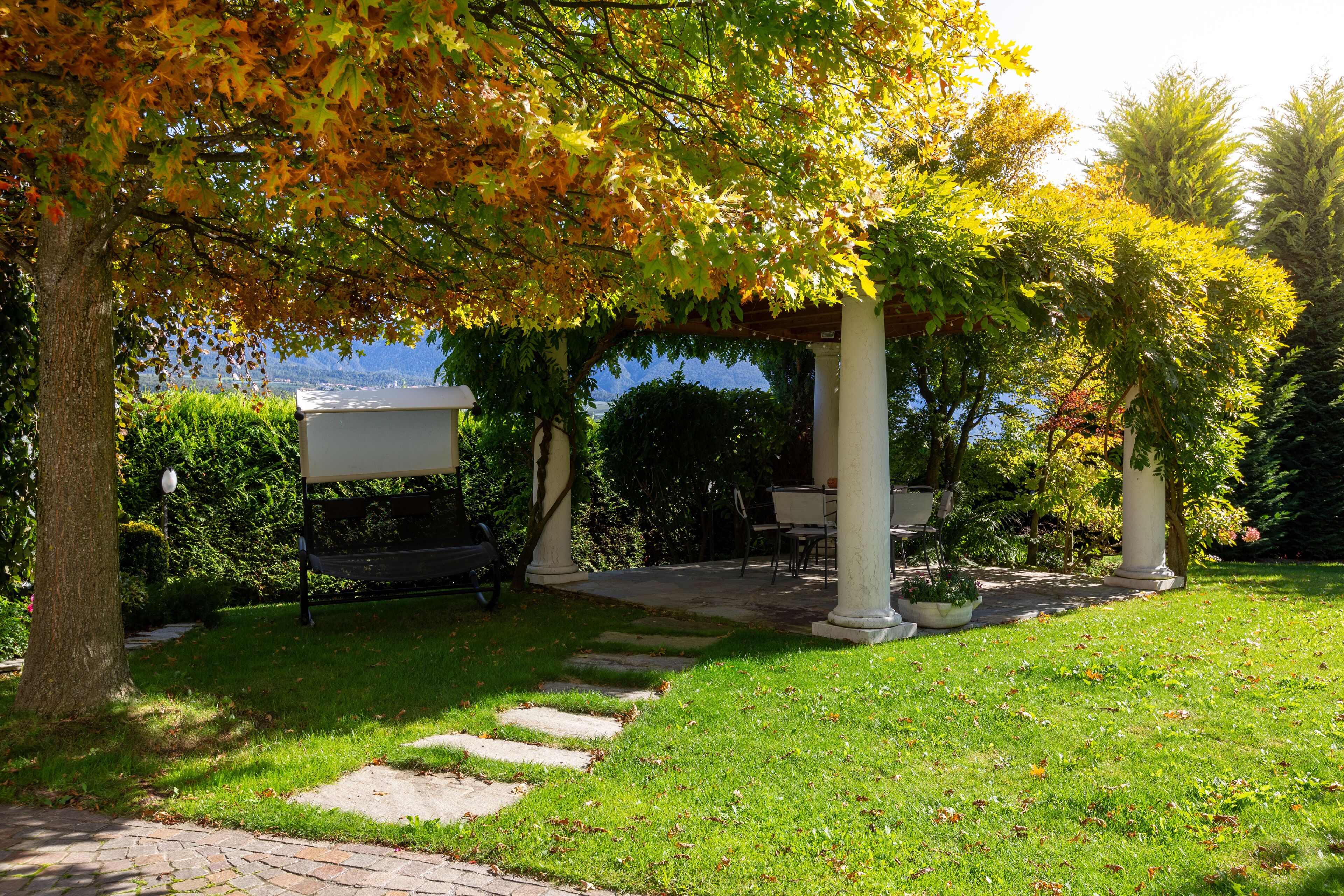 Un belvédère avec un banc, entouré d’un jardin bien entretenu et agrémenté d’un sentier en pierre.
