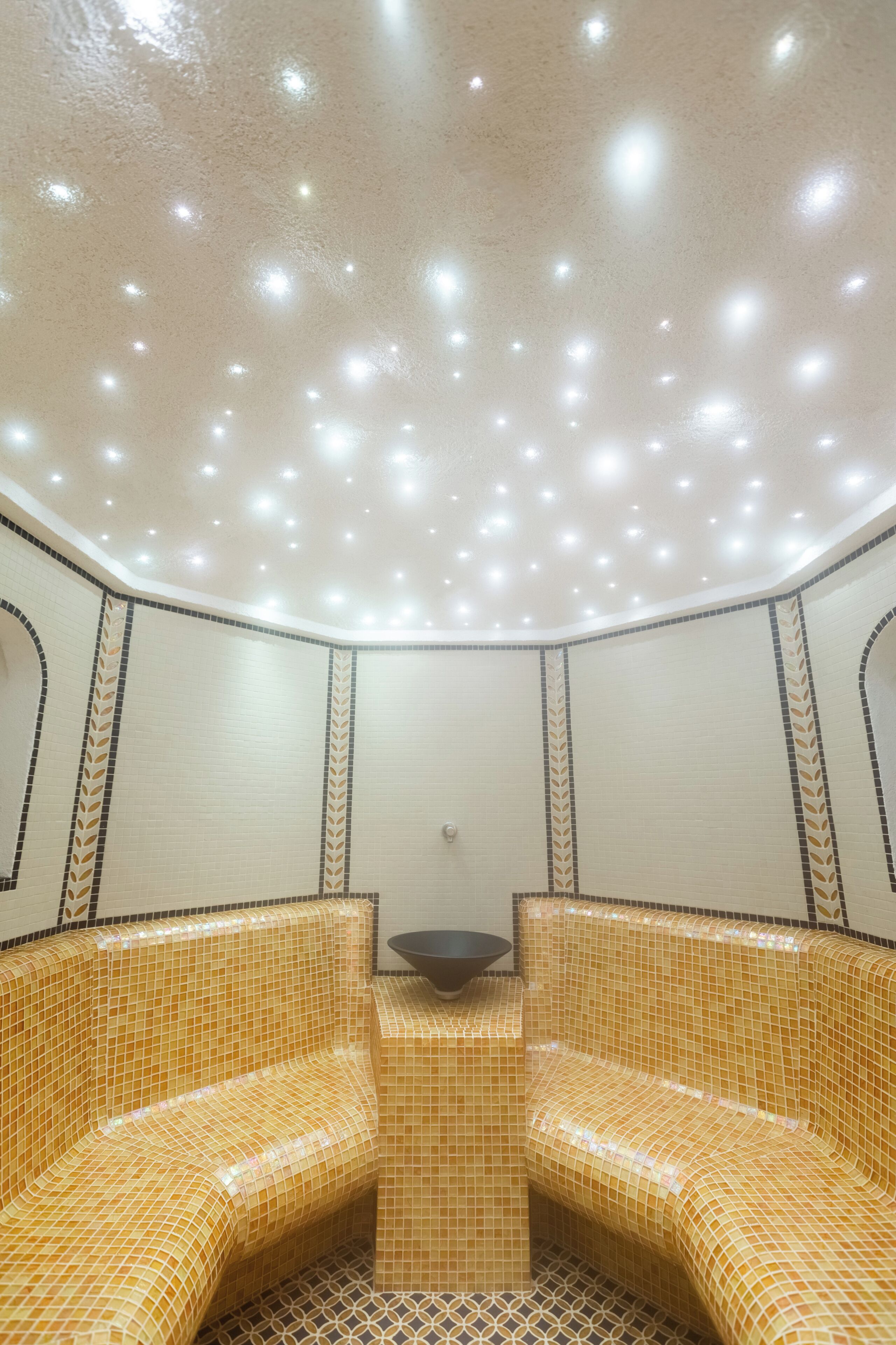 A room with a tiled floor, a central seating area with a bowl, and a ceiling with recessed lighting.