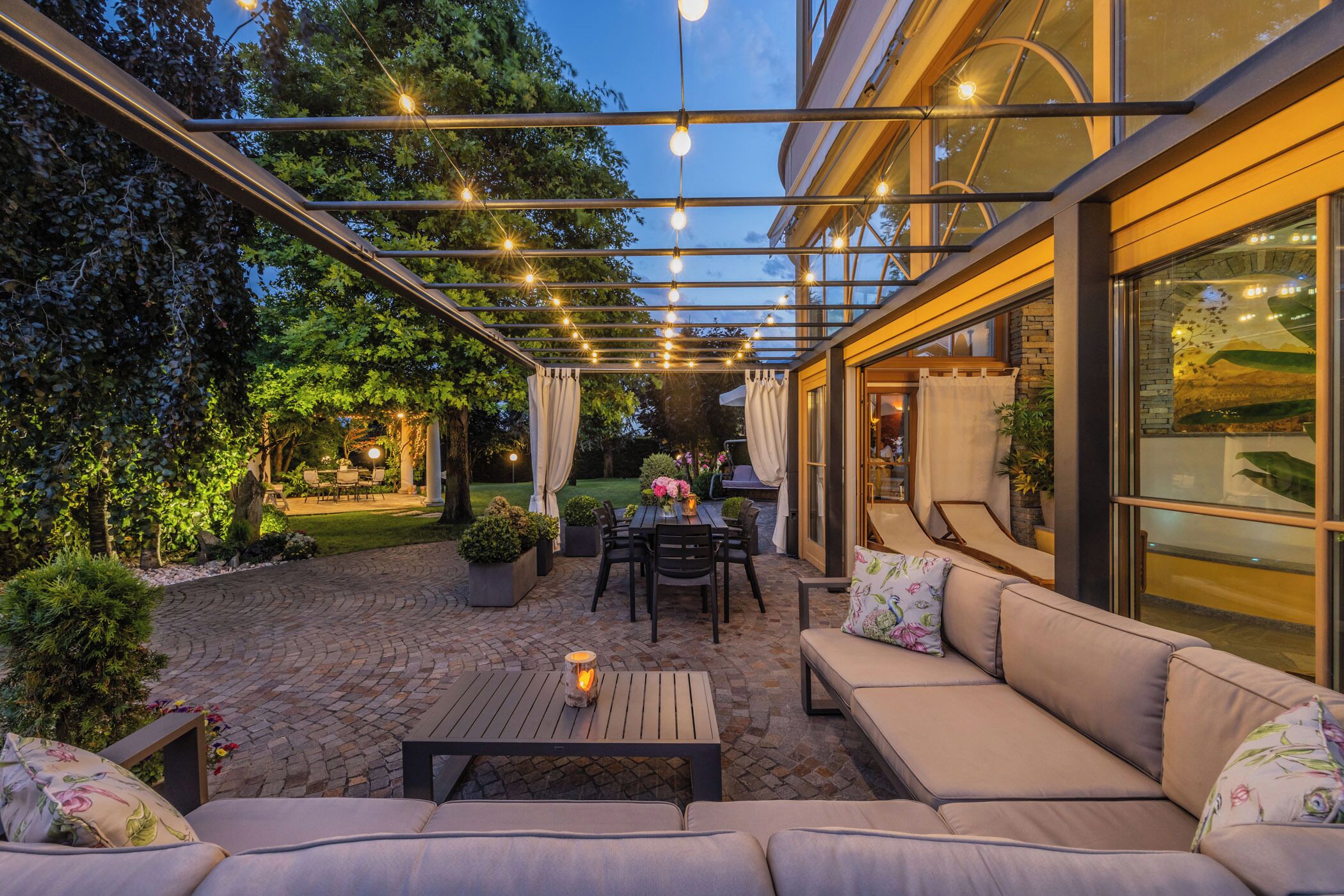 An outdoor patio with a covered seating area, a table with chairs, and a view of the garden.