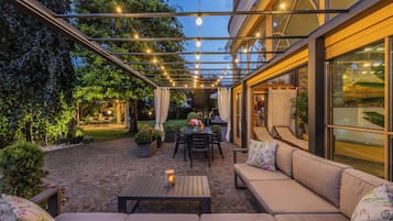 An outdoor patio with a covered seating area, a table with chairs, and a view of the garden.
