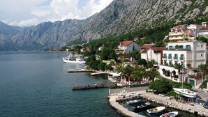 A coastal town with a marina, buildings with balconies, and a mountainous backdrop. - Forza Mare (Kotor)