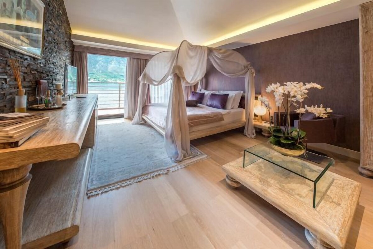 Un dormitorio con cama a dosel, una mesita de noche, una mesa de centro de cristal y vistas al exterior.