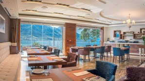 A dining area with tables set for a meal, a sofa, and a view of a mountainous landscape. - Forza Mare (Kotor)