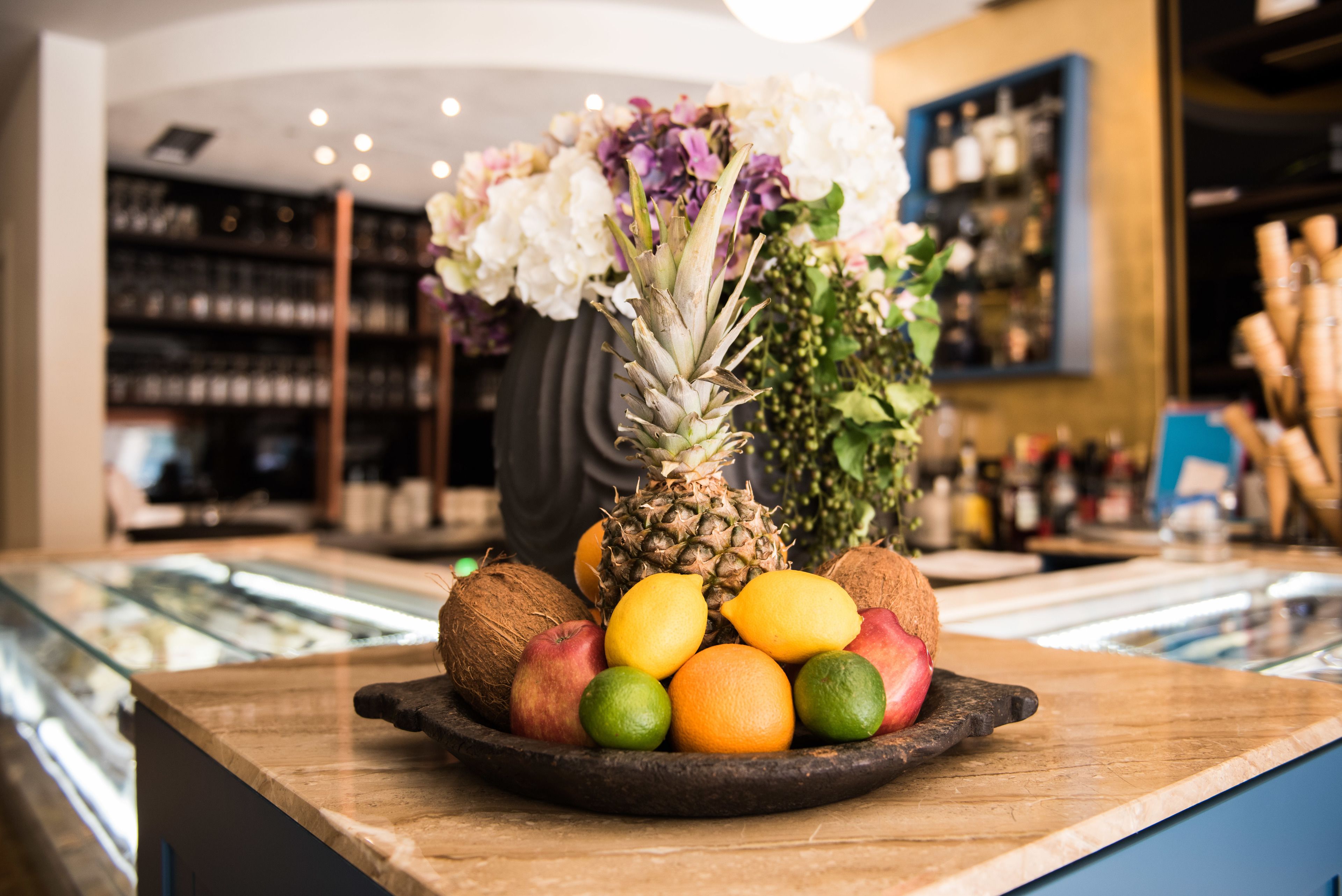 Una ciotola di frutta con ananas, mele, arance e lime su un bancone di legno.