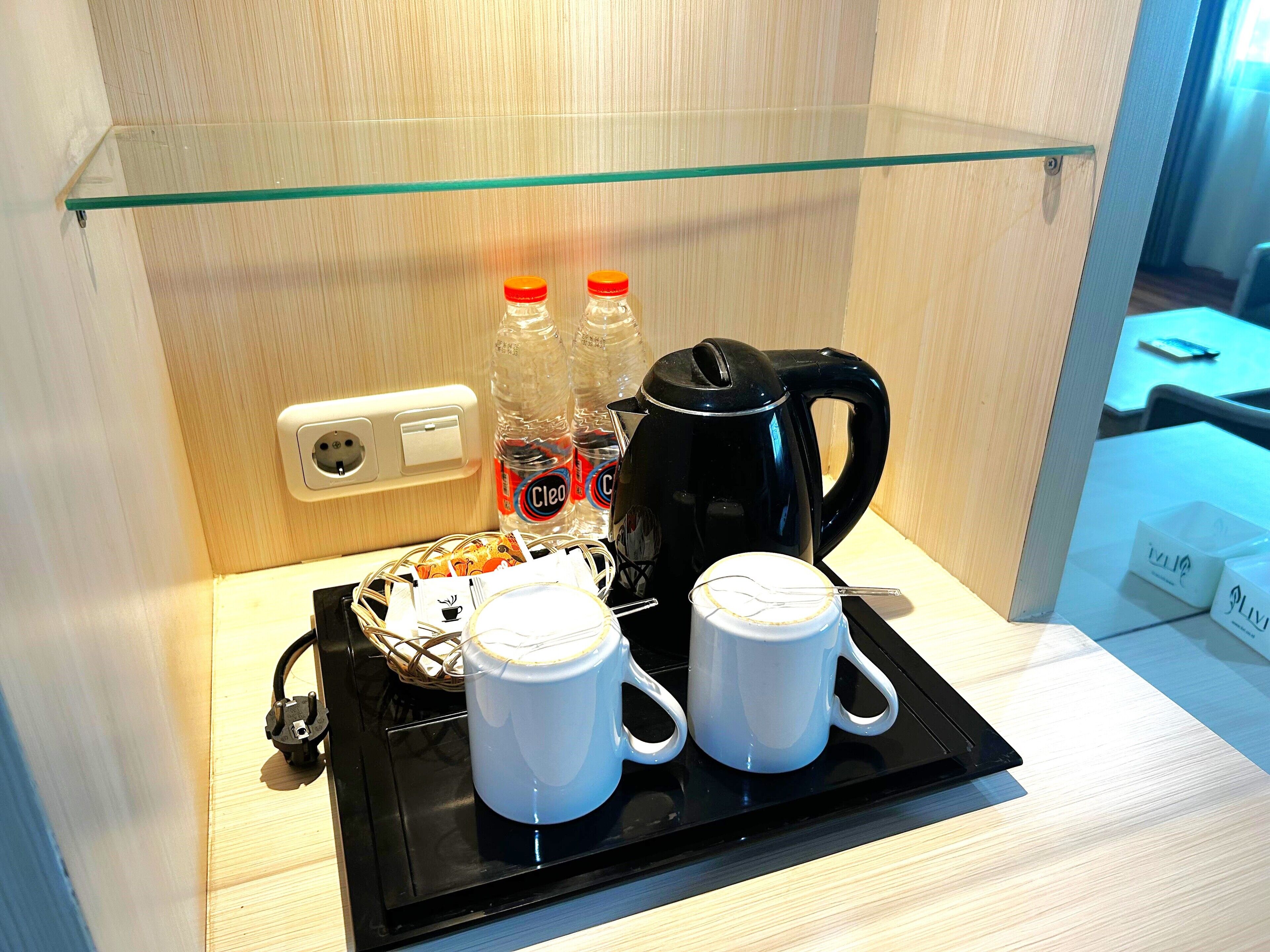A hotel room with a glass shelf containing a coffee maker, two white mugs, and two bottles of water.