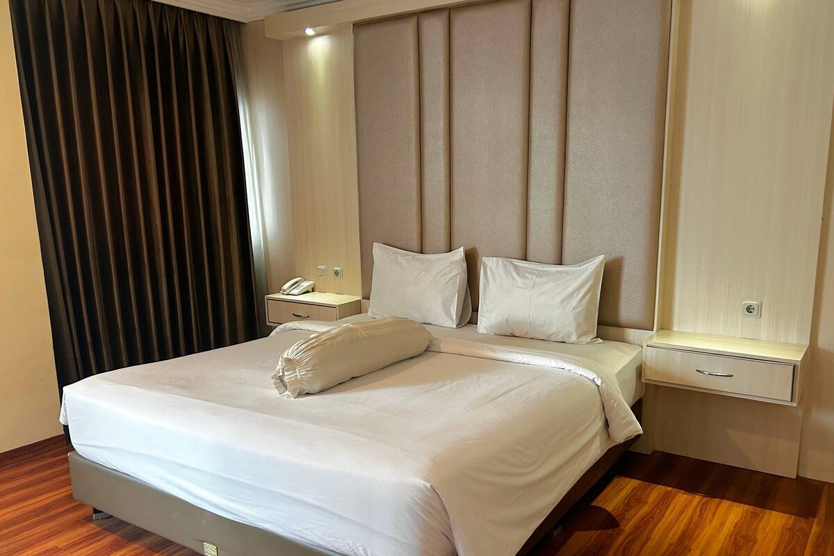 A modern hotel room with a large bed, a bedside table with a phone, and a nightstand.