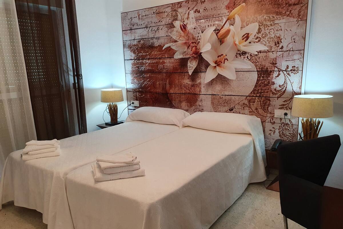 Un lit bien fait, avec du linge de lit blanc, une œuvre d’art florale sur la tête de lit et deux lampes de chevet.