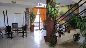 A spacious living area with a dining table, chairs, a staircase, and multiple potted plants. - Hotel La Palmera (Valverde del Fresno)