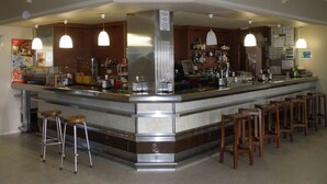 A bar area with a counter, stools, and hanging pendant lights. - Hotel La Palmera (Valverde del Fresno)